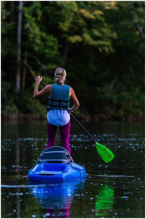 A woman enjoys stand-up kayaking on a calm lake su