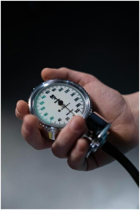 A hand holding a sphygmomanometer showing blood pr