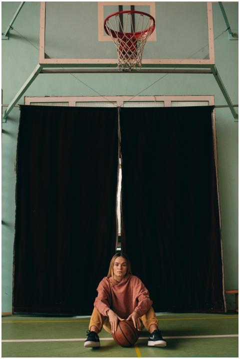 A young woman sits on an indoor basketball court h