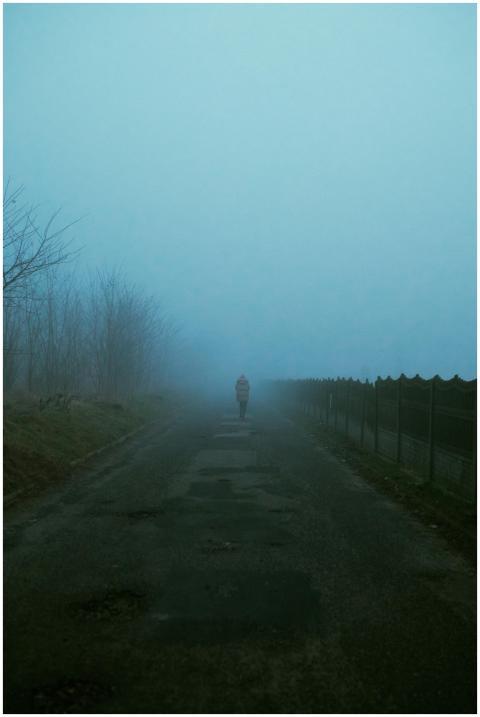 Lonely person walking on a foggy, deserted road at