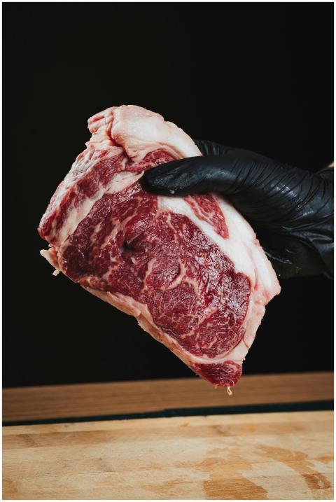 Close-up of a raw ribeye steak held by a gloved ha
