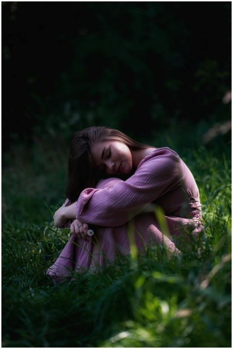 A young woman in a pink dress sits peacefully in a