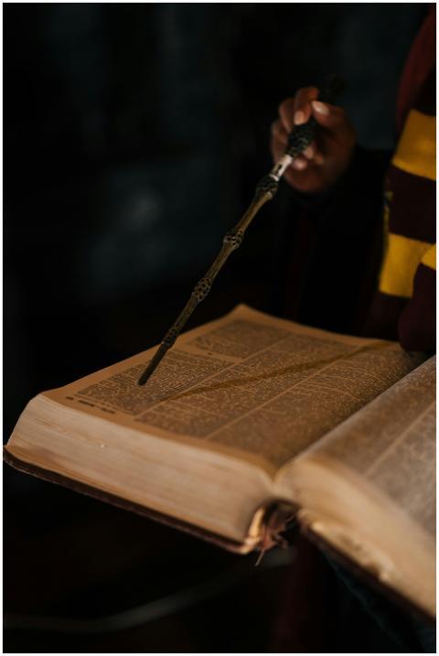 Hand points a wand at an ancient book, suggesting