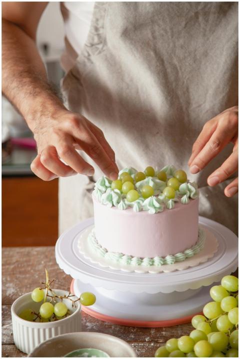 Close-up of hands decorating a pastel cake with gr