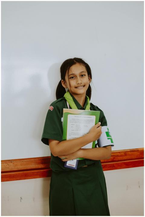 Girl scout in green uniform holding notebooks, sta