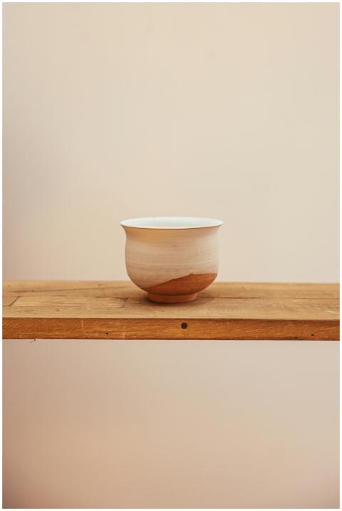 A simple ceramic bowl placed on a wooden shelf wit