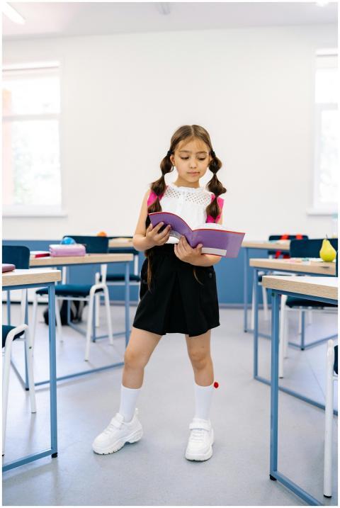 A young girl standing in a classroom reading a boo