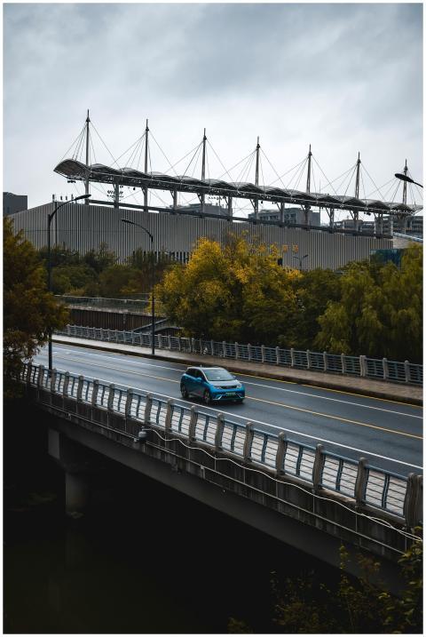 A blue car travels on a bridge with a stadium back