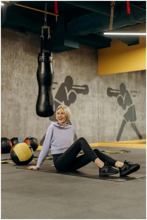 A woman relaxes on a gym floor surrounded by boxin