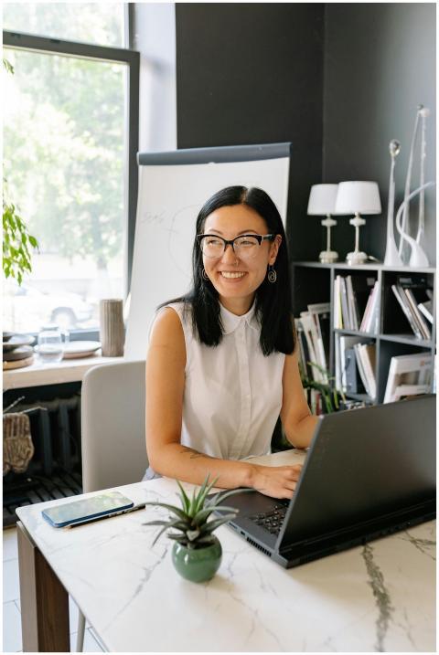 Smiling Asian businesswoman using laptop in a styl