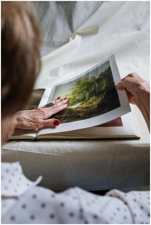 An elderly woman turns pages of a landscape art bo