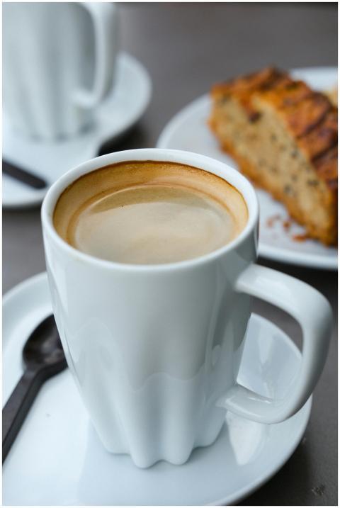 A steaming cup of coffee with a slice of cake on a