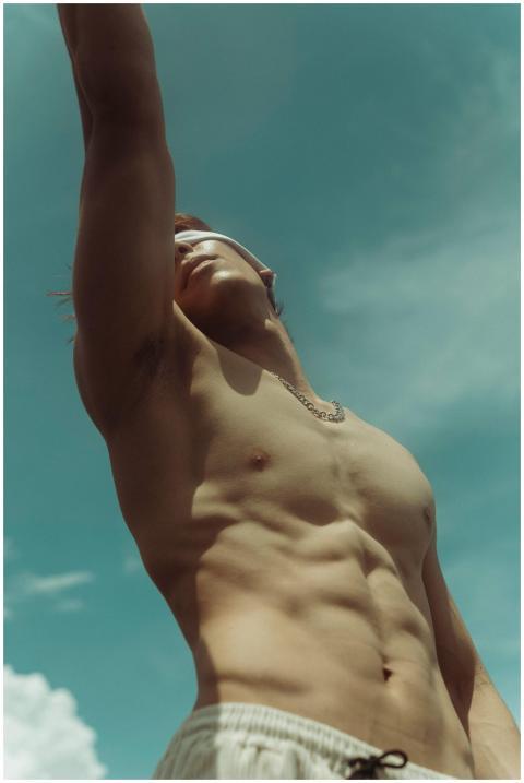Shirtless man reaching upwards under a clear summe