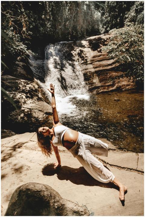 Pregnant woman doing yoga pose near a scenic water