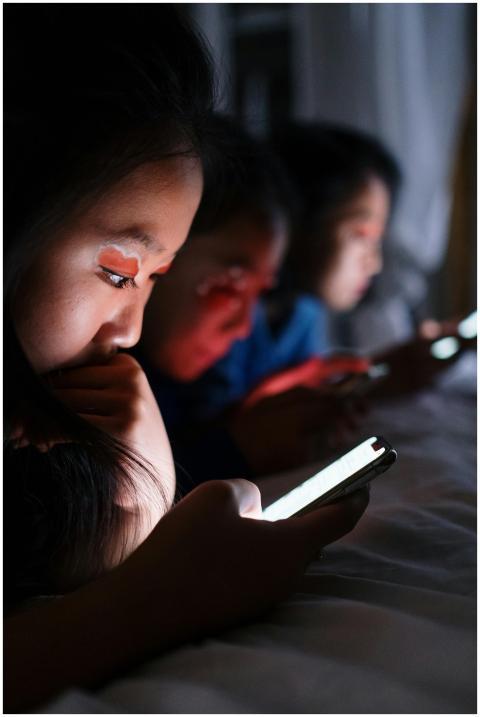 Three teenagers using smartphones in bed at night,