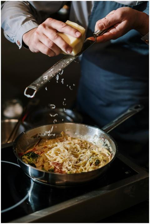 A chef in apron grates cheese onto pasta in a mode