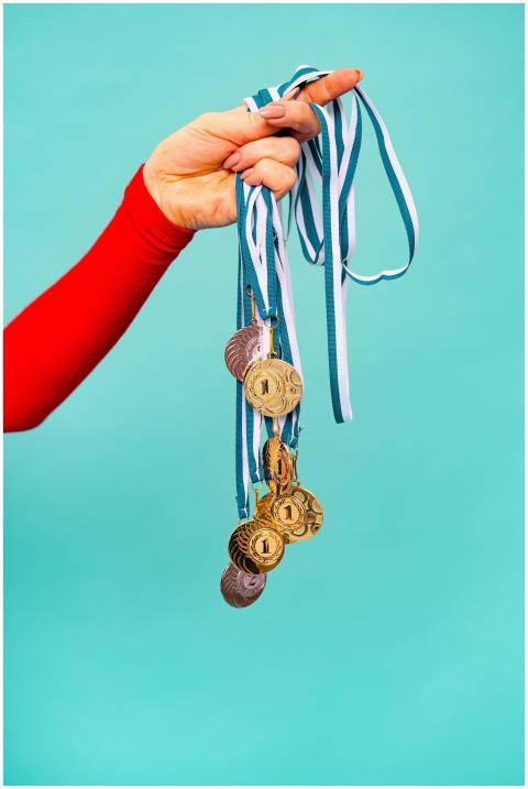 A hand holds several gold medals with ribbons, sym