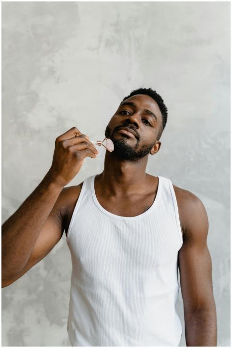 Portrait of a young man using a jade roller for fa