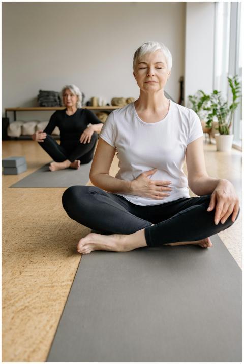 Two senior women meditating indoors on yoga mats w