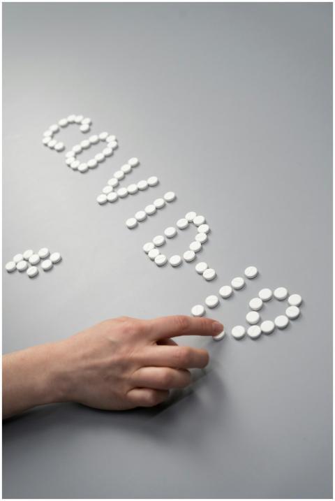 Hand arranging white tablets to spell COVID-19, em