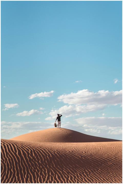 A lone figure stands atop a sand dune under a vast