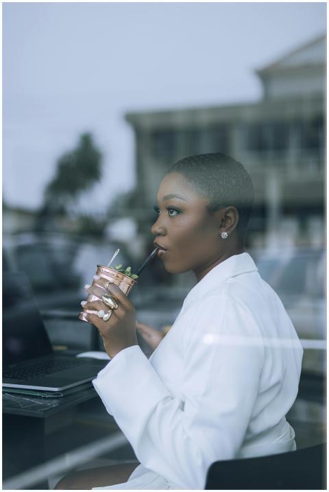 Stylish woman in white sipping a drink while worki