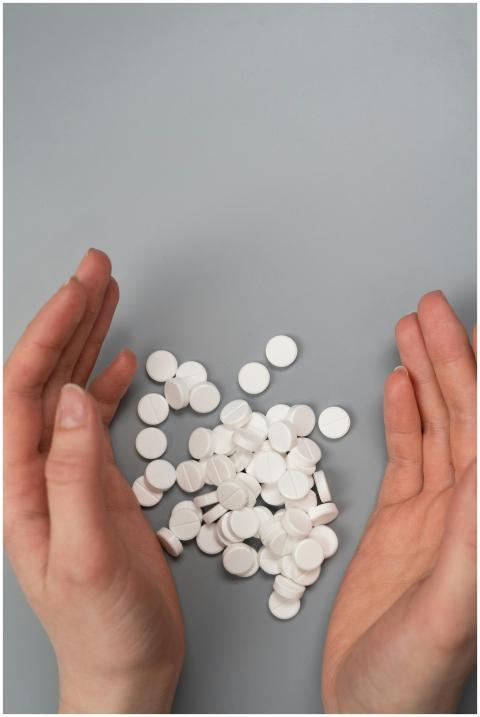 A close-up of hands surrounding white pills on a g