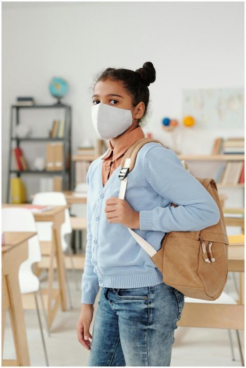 Girl with backpack in classroom, wearing face mask