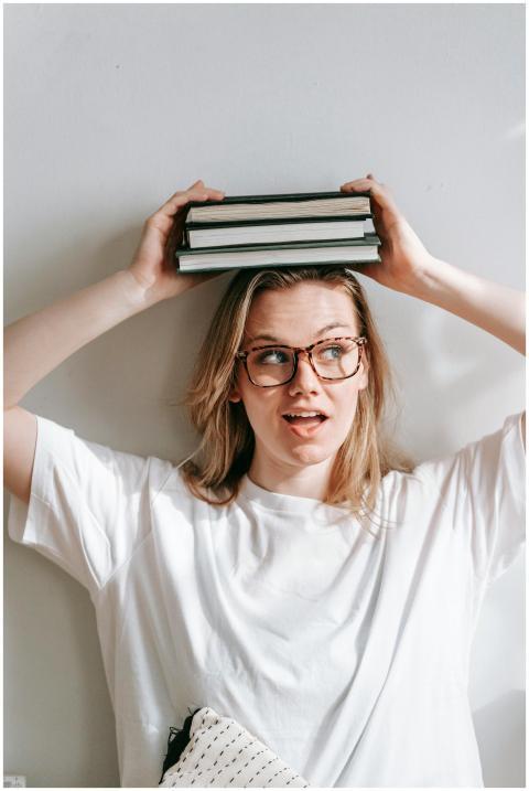 Playful young woman with glasses balancing books o