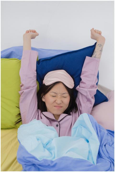 An adult woman waking up in colorful bedding, stre