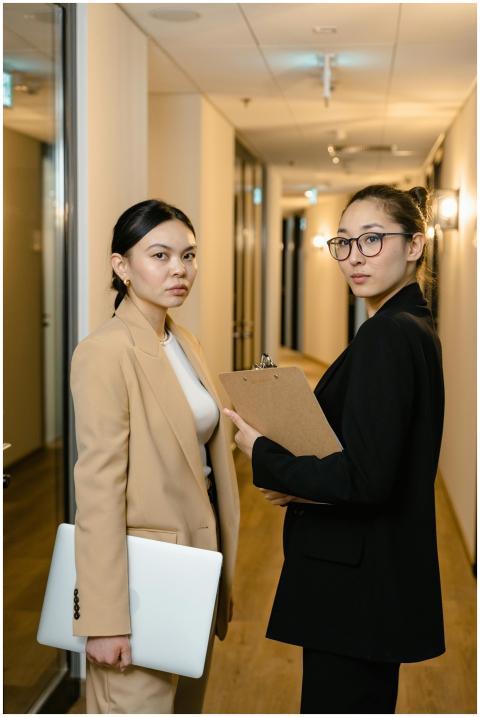 Two businesswomen in formal attire standing in a h
