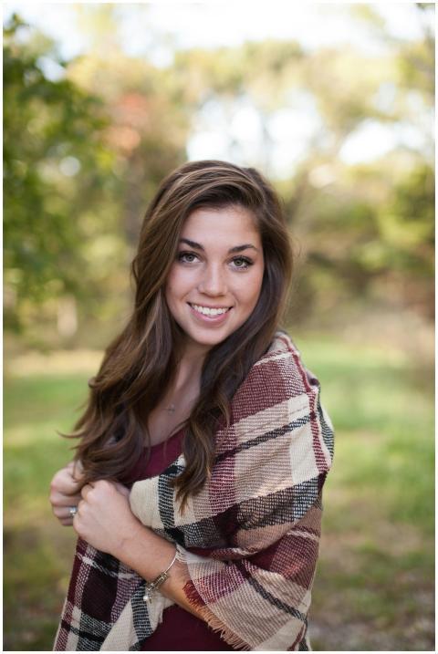 A woman smiling outdoors with a cozy plaid shawl,