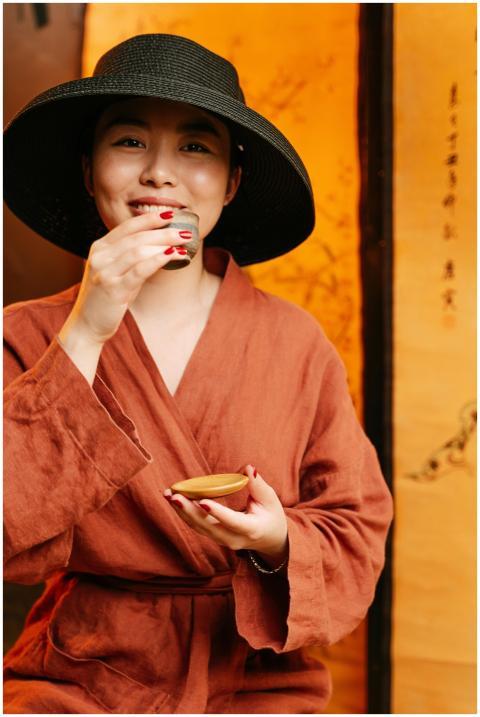 East Asian woman in robe and hat enjoying a tea ce