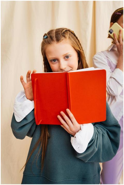 A young girl with braided hair reads a bright red