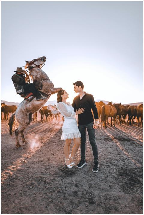 A couple embraces in a rural field with horses und