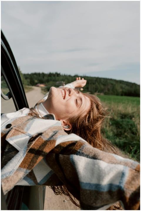 Joyful young woman leans out of car window, embrac