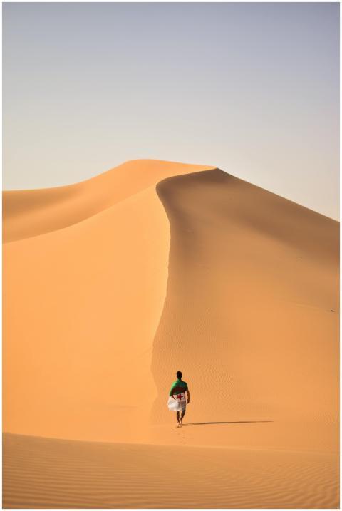 A lone traveler walking over the vast, golden sand