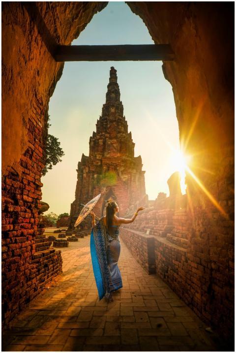 A woman in traditional wear stands with an umbrell