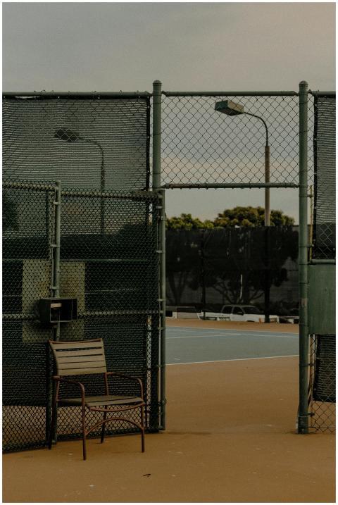 A deserted tennis court with a wire fence and a so