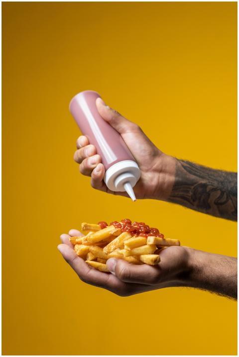 A person pours ketchup onto crispy French fries ag