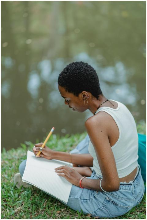 Focused woman writing notes by a serene lakeside.
