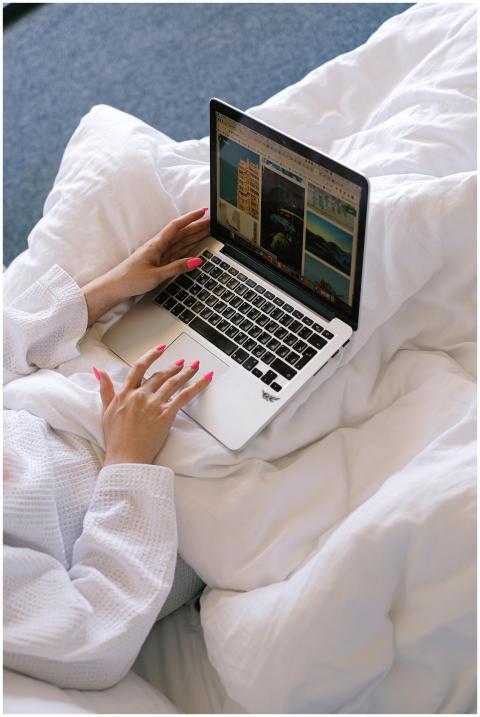 A woman in white bathrobe working on a laptop in b