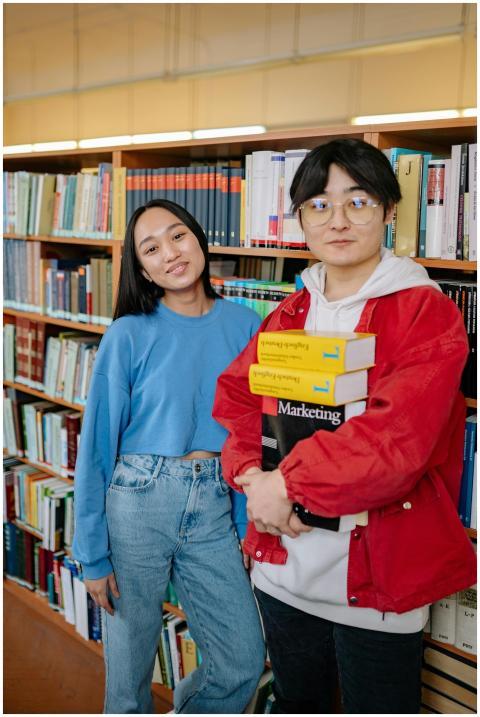 Two students smiling and holding books in a librar
