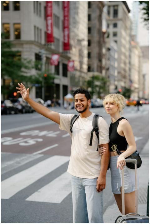 Young couple with luggage hailing a taxi on a busy