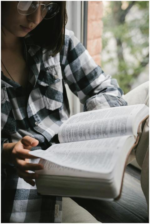 A woman wearing glasses reads an open book by the