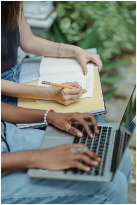 Two women studying outdoors with a laptop and note