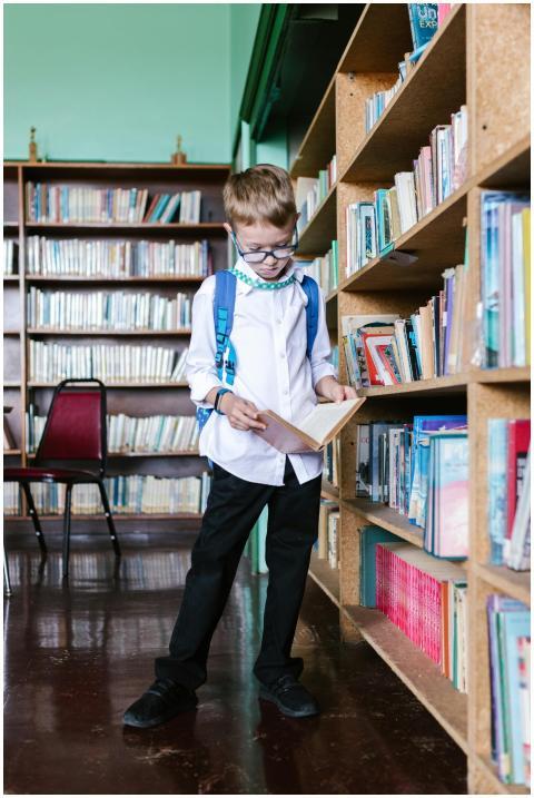 A child in a library explores books, wearing a bac