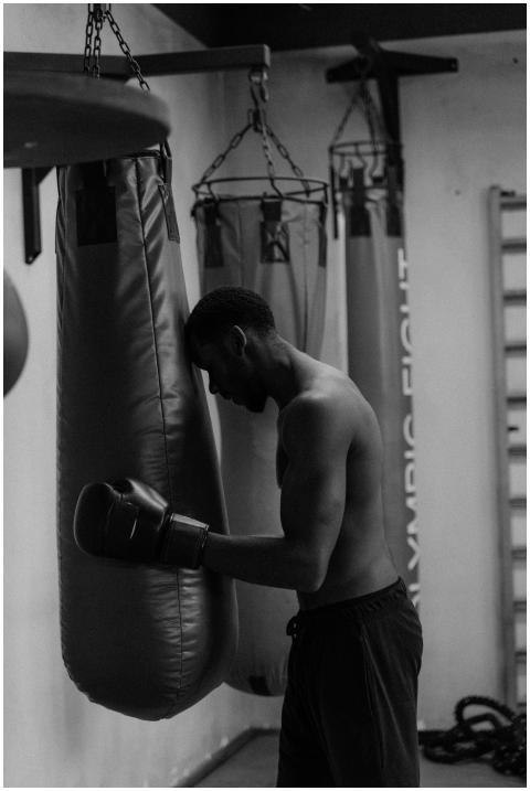 A shirtless boxer leans on a punching bag, showcas