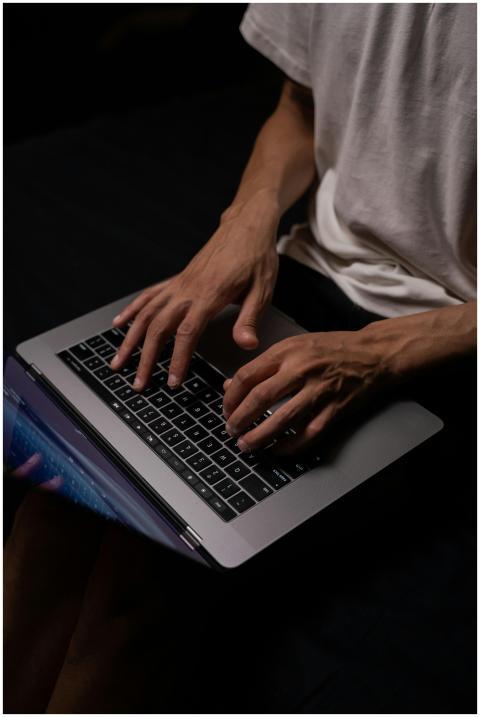 An adult male programmer typing on a laptop in a d