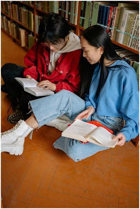 Two students sitting on library floor reading book